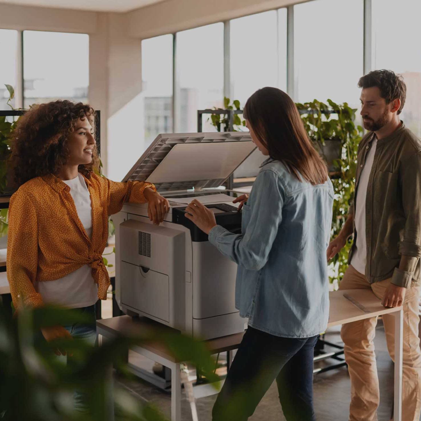 Colleagues collaborating at a large commercial office printer, demonstrating Dragonfly Tech's managed print services and hardware solutions.